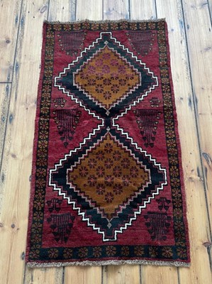 Lot 556 - A Baluchi rug, having two lozenges on a red...